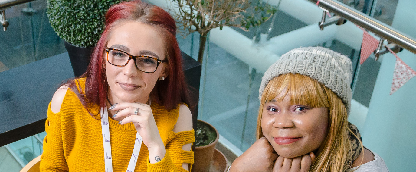Our young inspection volunteers Toni and Raysa. Toni has red hair and is wearing a yellow jumper and glasses. Raysa has blonde hair and is wearing a grey hat. They are both looking up to the camera smiling. 